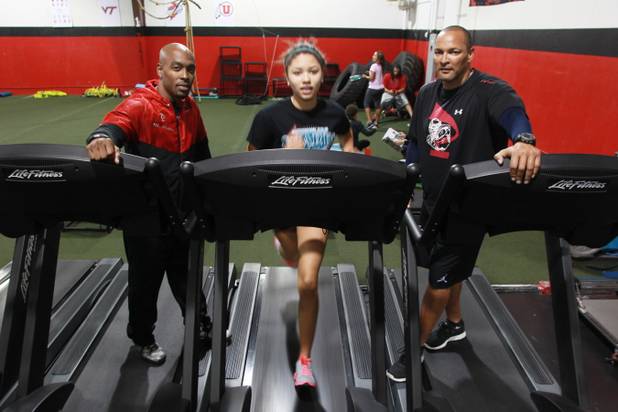 Phase 1 Sports owners Mike Waters, left, and Mel Spicer stand on either side as Silvestri Middle School student Mariah Morris works out on a treadmill. Phase 1 helps local athletes go to college and receive scholarships.